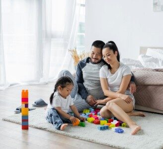 cheerful asian parents looking at toddler daughter playing building blocks